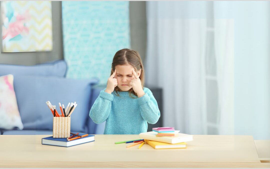 Girl sitting at a table with fingers pointing to her head at her temples with her eyes closed trying to think