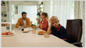 Family sitting at dinner table with parents talking and boy with hand in his head looking away